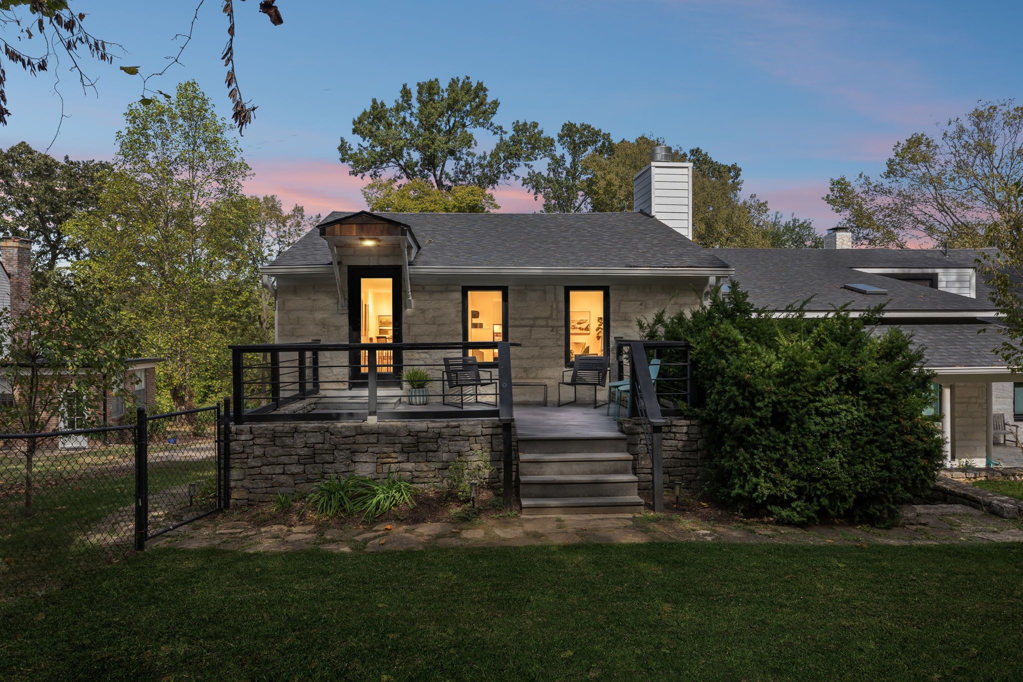 A two-story house with a stone facade, a covered porch, and a staircase leading to the entrance.