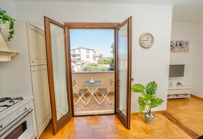 Ein Zimmer mit einer Schiebeglastür, die auf einen Balkon führt, einem weißen Herd, einem Esstisch mit Stühlen und einer Topfpflanze.