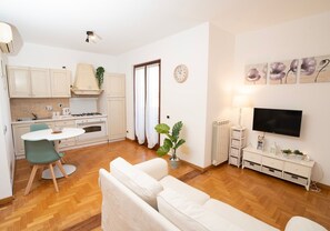 Eine moderne Wohnung mit Küchenzeile, Essbereich, Wohnzimmer mit Sofa, Fernseher und einer Pflanze.