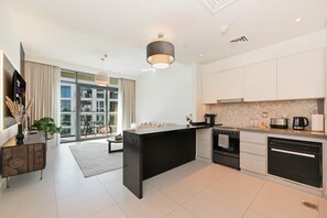 A modern kitchen with a central island, black and white cabinetry, and a large window providing a view of the cityscape. - Premium 1BR - Creek Harbour - Pool, Sea View (Dubai)