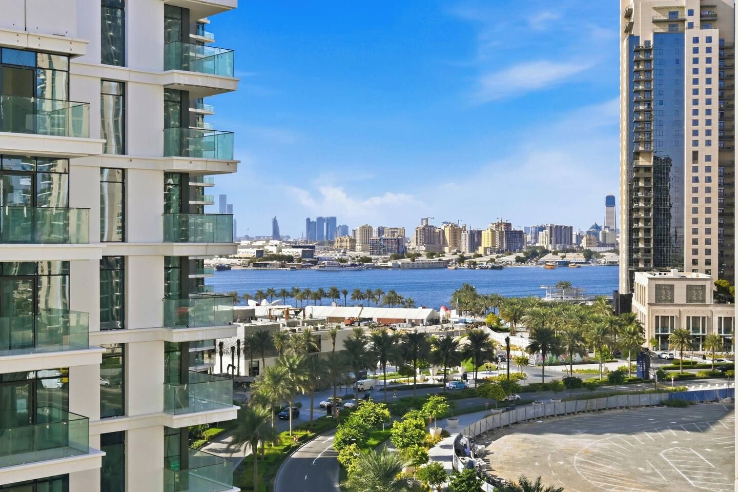 A modern high-rise building with multiple balconies overlooking a marina and city skyline.