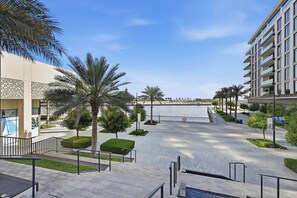 A modern building with a flat roof, a paved walkway, and palm trees. - Premium 1BR - Creek Harbour - Pool, Sea View (Dubai)