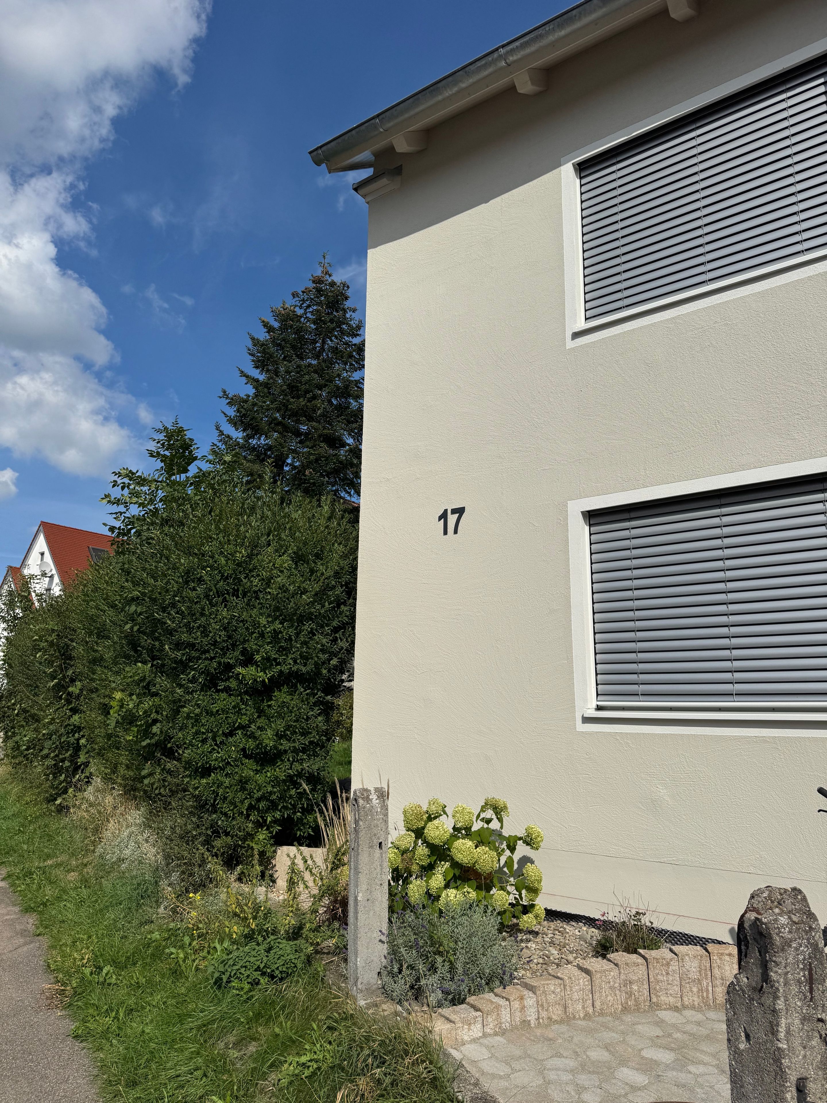 Een gebouw met twee verdiepingen, een beige gevel en nummer 17, met een raam met gesloten zonwering.