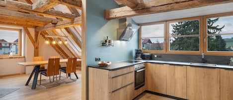 Una cocina moderna con vigas de madera, un comedor con mesa y sillas, y vistas amplias por grandes ventanas.