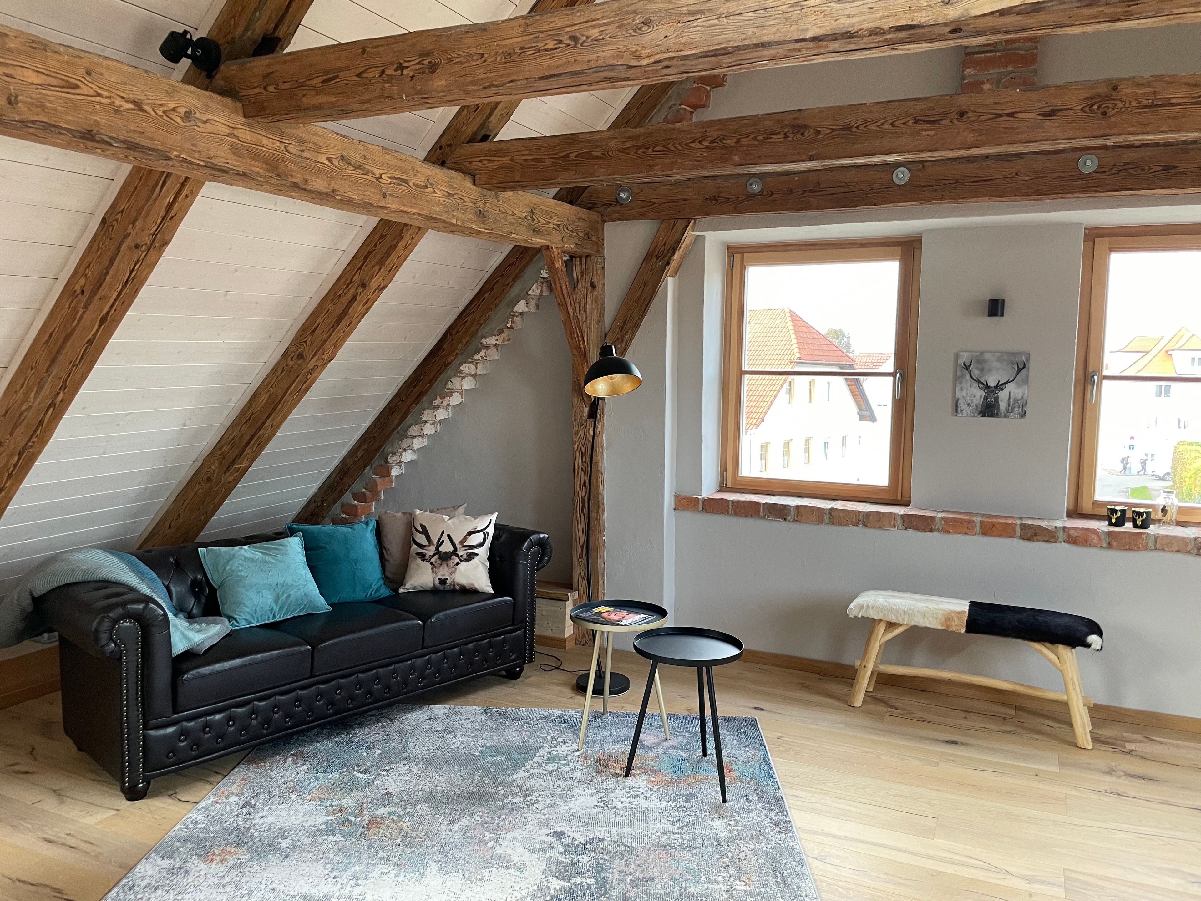 Une pièce de style loft avec des poutres en bois apparentes, un canapé en cuir noir, une petite table ronde et un banc.