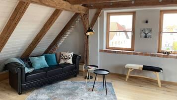 Une pièce de style loft avec des poutres en bois apparentes, un canapé en cuir noir, une petite table ronde et un banc.