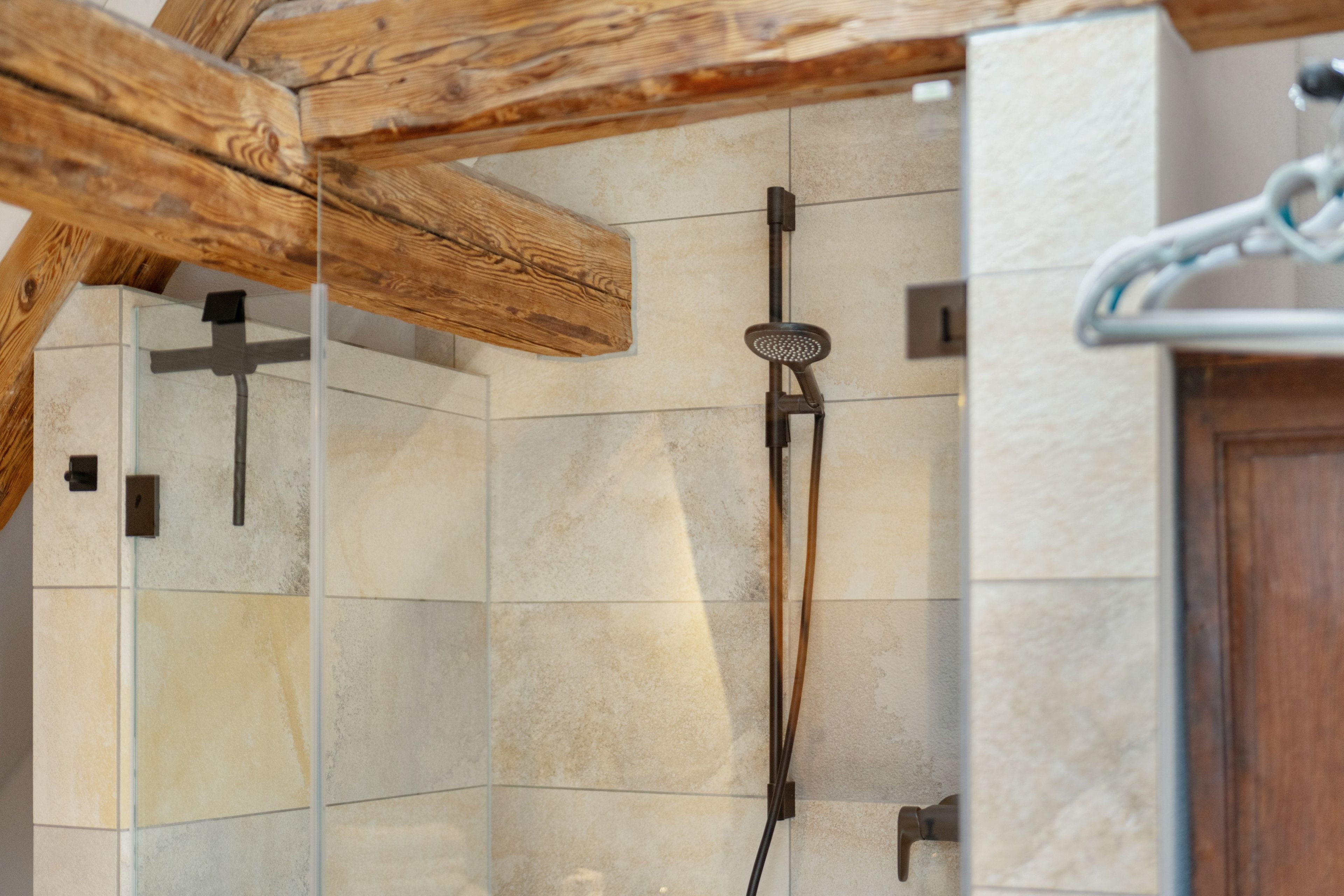 A shower with a handheld showerhead, a glass enclosure, and a wooden ceiling beam.