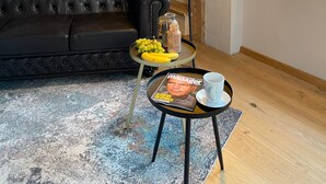 A loft-style room with exposed wooden beams, a black leather sofa, a small round table with a magazine, a lamp, and a window with a view. - DG Apartment alpenchic with Balcony in Ottobeuren – Sleeps 2 (Ottobeuren)