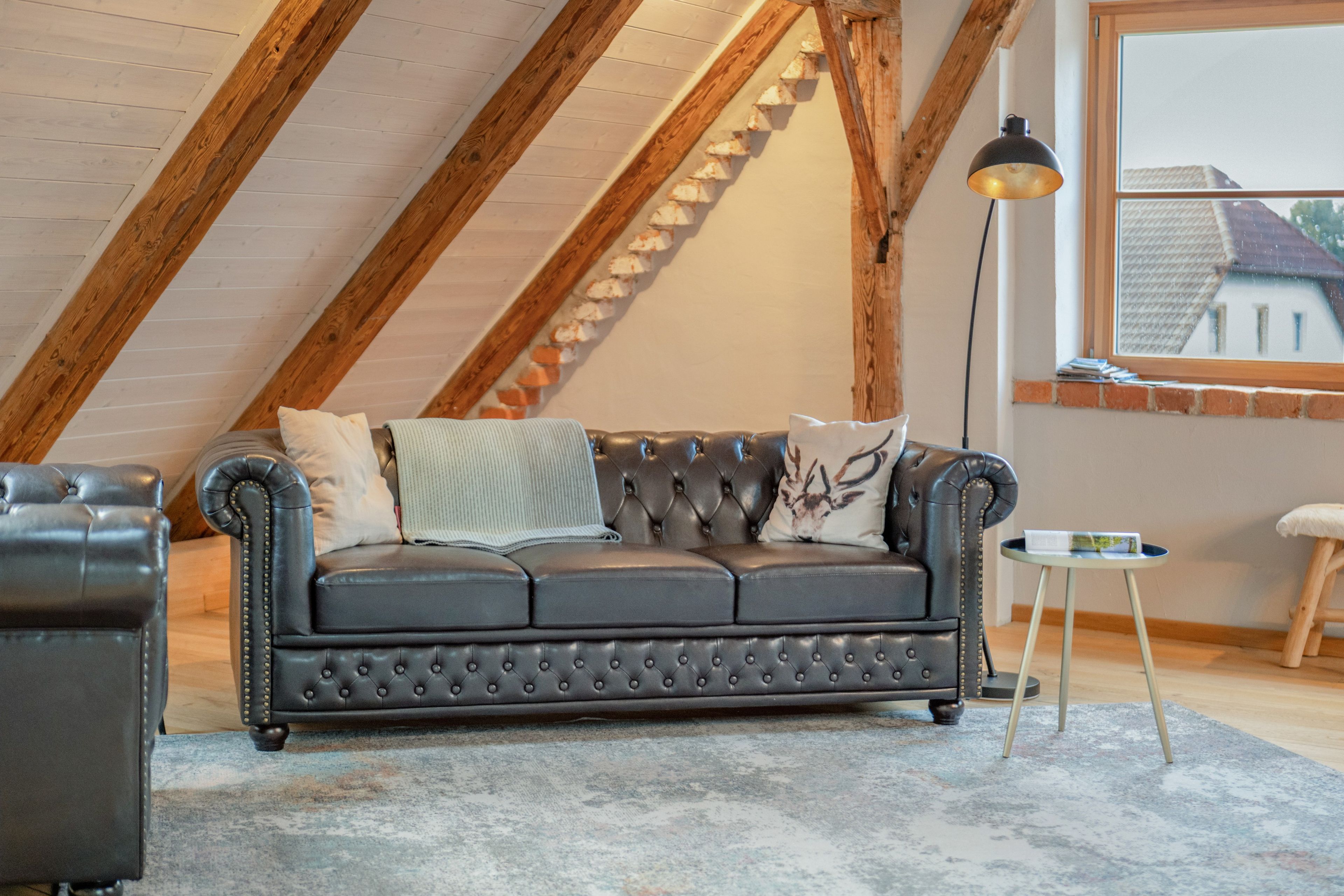 Un espacio tipo loft con un sofá de cuero oscuro, una mesita redonda y una lámpara de pie.