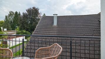 Ein Balkon mit Blick auf ein Gebäudedach, einem Metallgeländer und einem Korbstuhl.