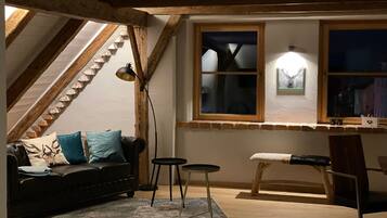 Ein gemütliches Schlafzimmer im Loft-Stil mit schrägem Dach, Holzbalken, einer schwarzen Ledersofa, einem kleinen runden Tisch und einem Holzsessel.