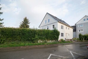 A residential building with a sloped roof, multiple windows, and a well-maintained hedge in front.