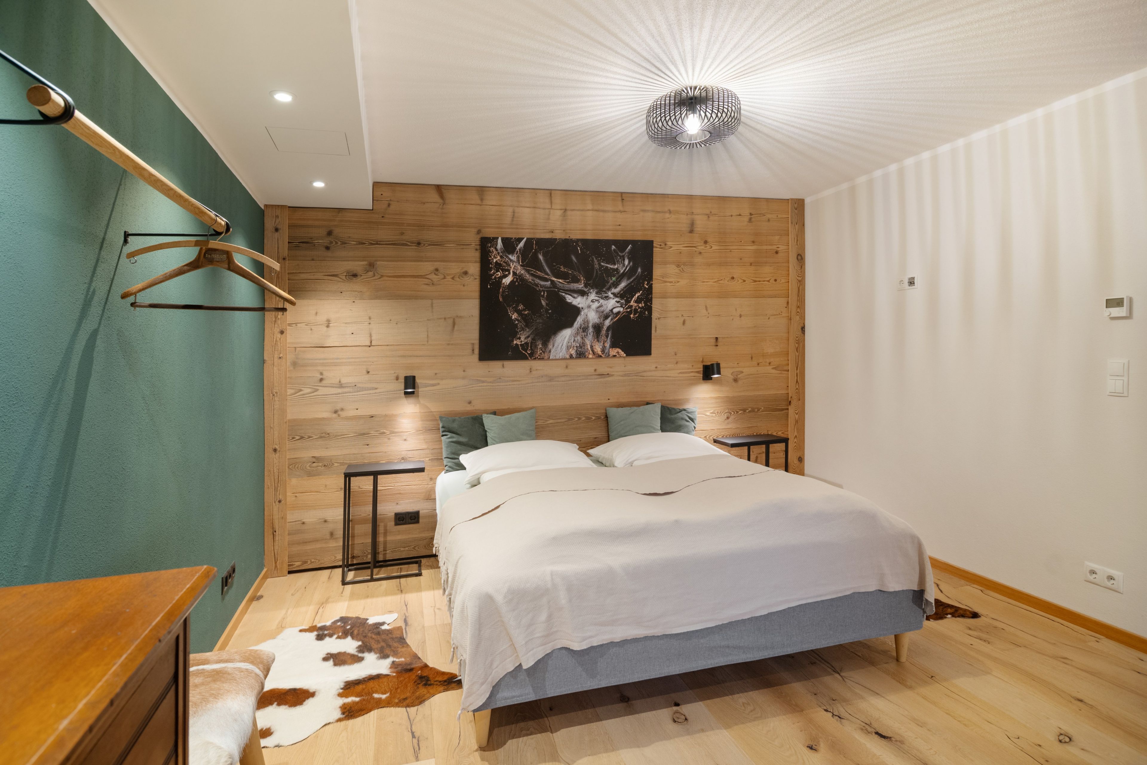 A modern bedroom with a wooden headboard, a large bed, a cowhide rug, and a wall-mounted light fixture.