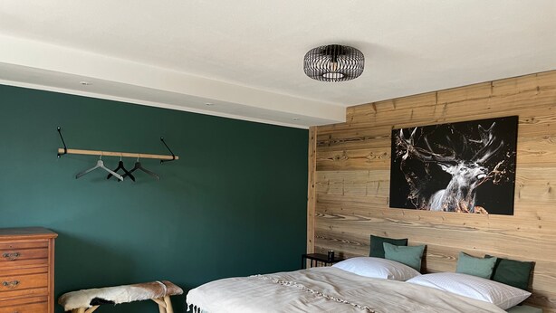 Un dormitorio con cama, cabecera de madera, lámpara colgante, un banco y un aparador.