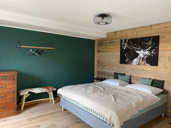 A bedroom with a bed, wooden headboard, a hanging light fixture, a bench, and a dresser. - Ground Floor Alpenchic Apartment with Garden and Terrace (Ottobeuren)