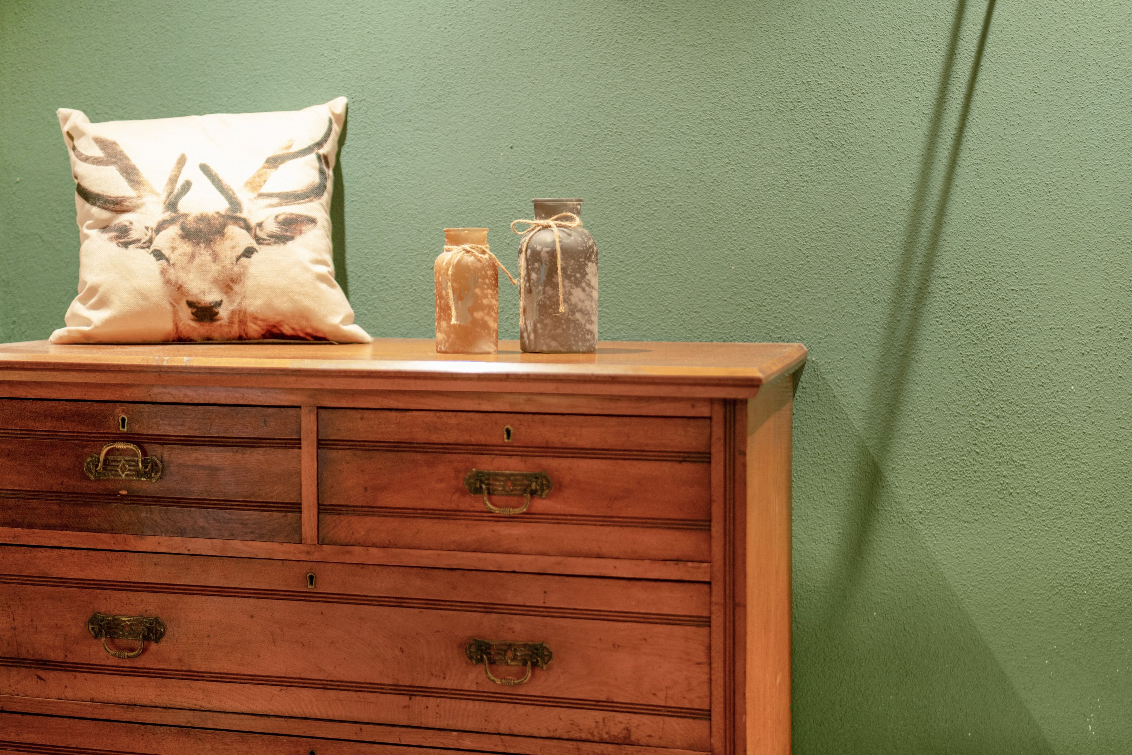 A wooden dresser with drawers and brass handles, topped with a pillow and two jars.