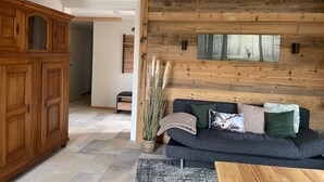 Una sala de estar moderna con un sofá gris oscuro, un revestimiento de pared de madera y un cuadro grande con una escena de bosque.