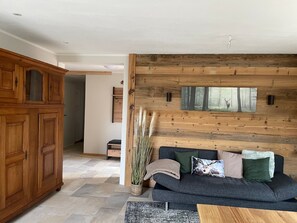 A modern living room with a dark grey sofa, wooden panel wall, and a large painting of a forest scene. - Ground Floor Alpenchic Apartment with Garden and Terrace (Ottobeuren)