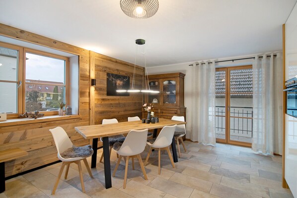 A wooden interior with a dining table, chairs, a cabinet, and a window with a view.