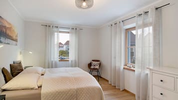 A bedroom with a bed, a chair, a dresser, and a window with curtains.