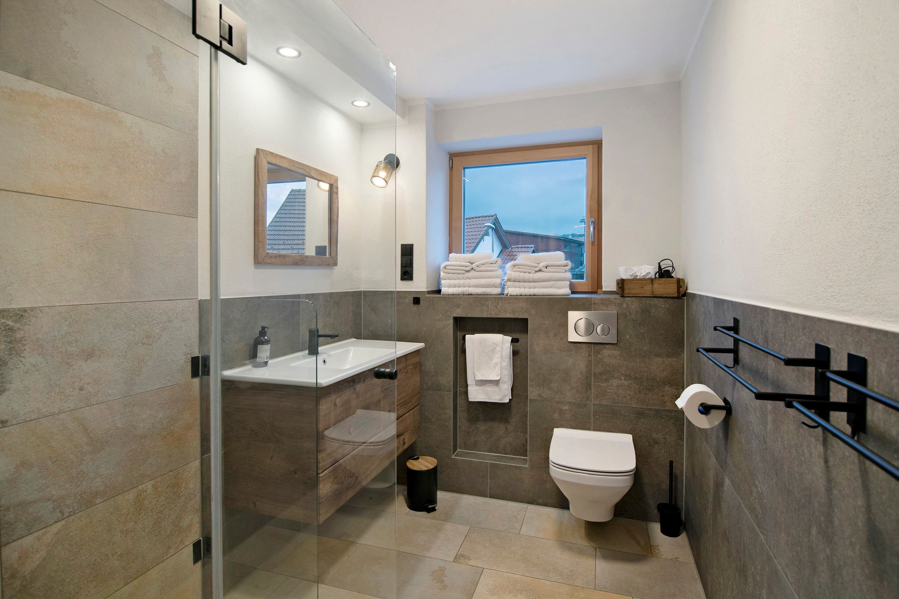 A modern bathroom with a glass shower enclosure, a sink, a toilet, and a window providing a view of the outside.