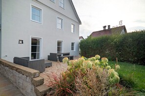A two-story house with a paved patio area, outdoor seating, and a well-maintained garden.