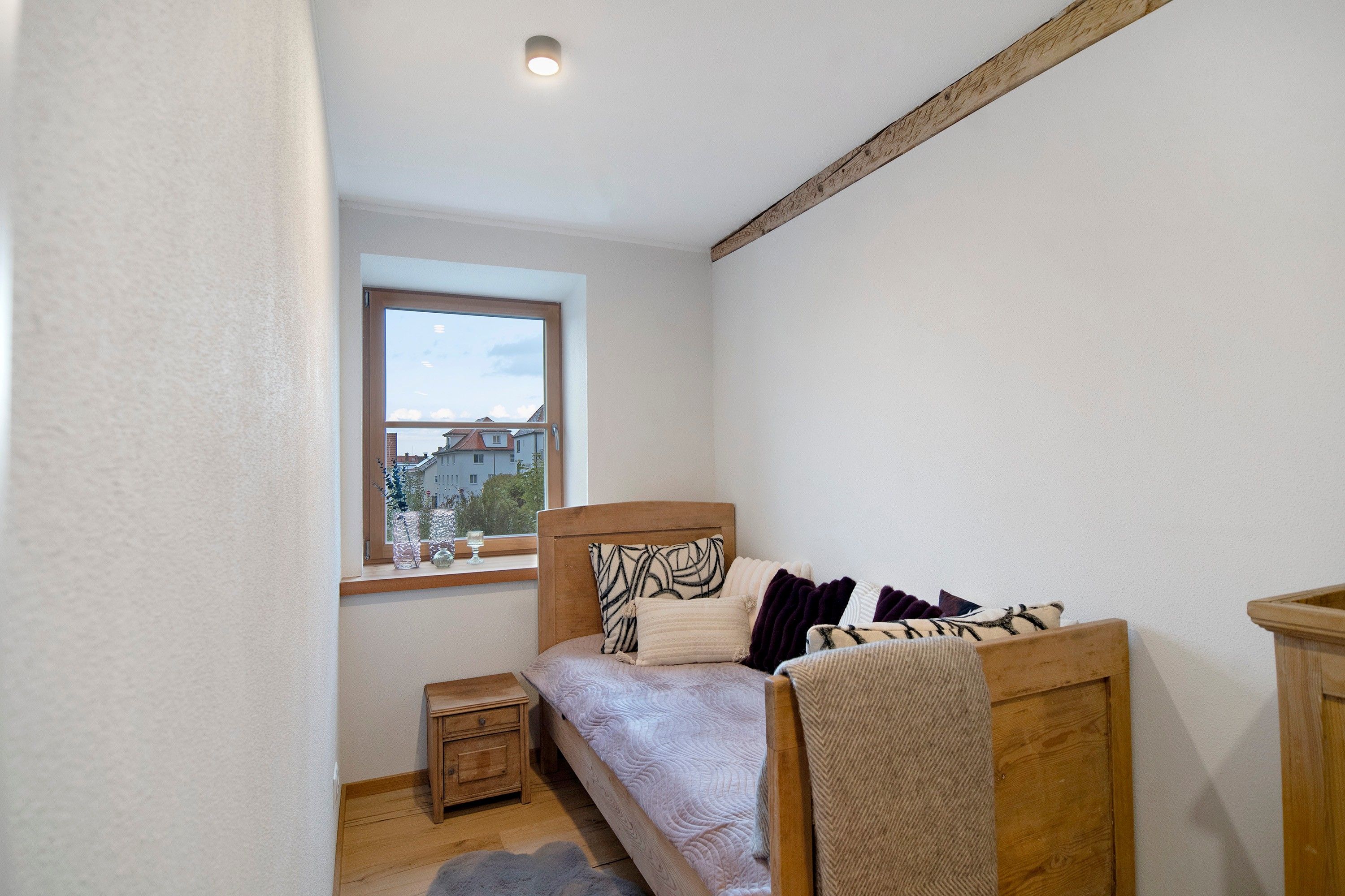 A bedroom with a wooden bed, a nightstand, a window with a view of buildings, and a ceiling light.