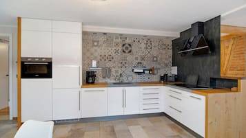 A modern kitchen with white cabinetry, a built-in oven, a coffee machine, and a patterned backsplash.
