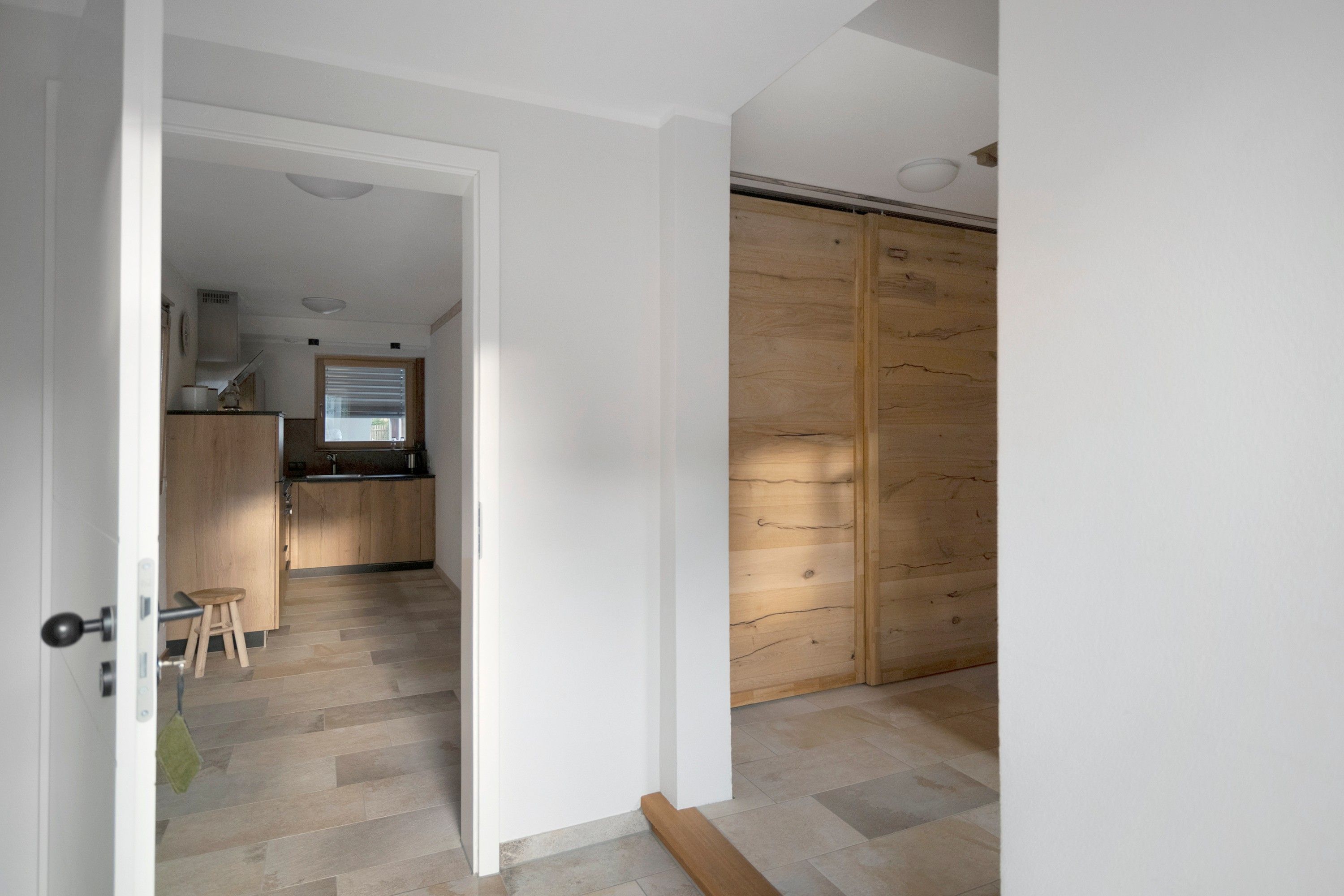 A room with a wooden floor, a kitchen area with wooden cabinets, and a sliding door.