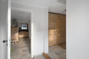 A room with a wooden floor, a kitchen area with wooden cabinets, and a sliding door.