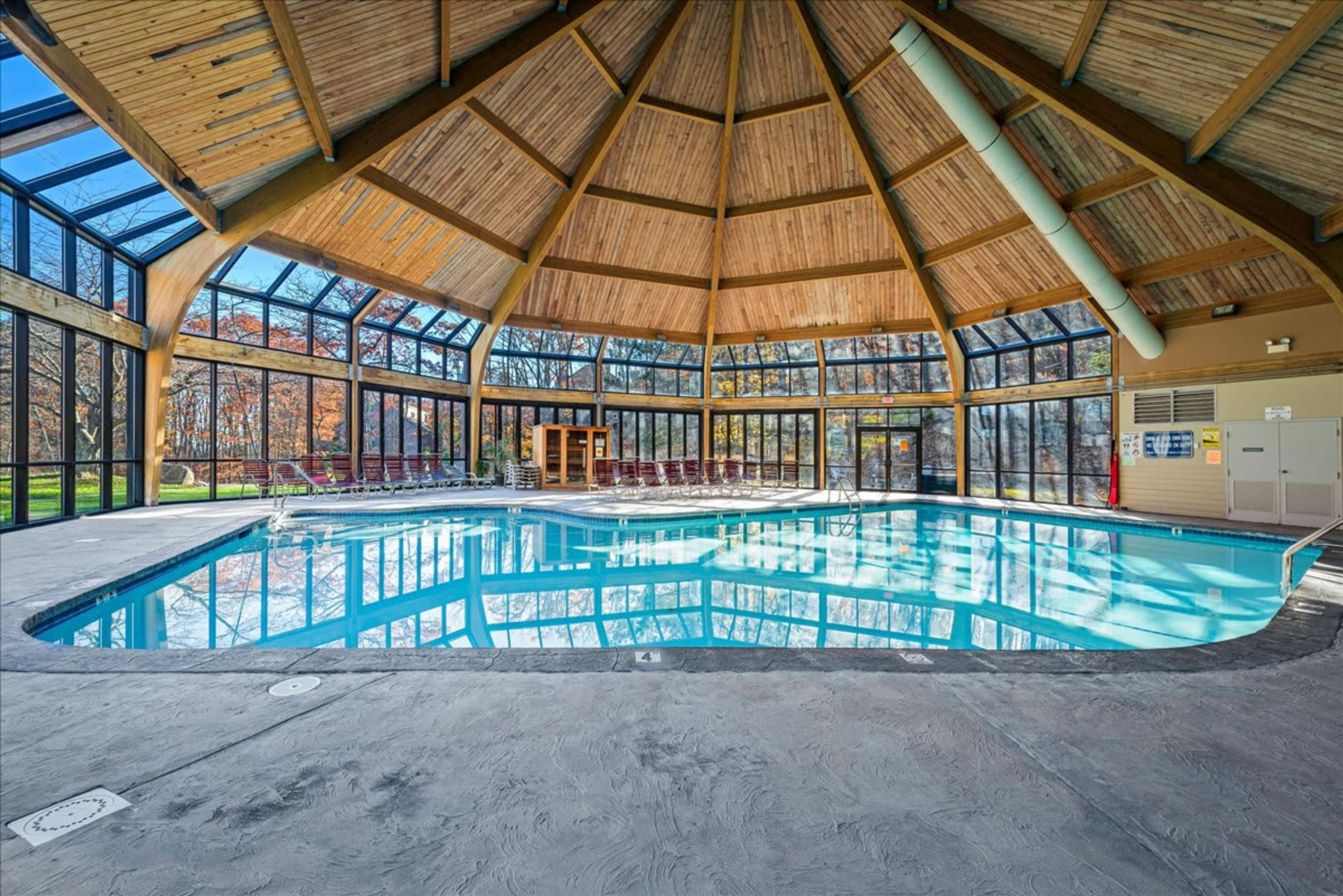 An indoor swimming pool with a wooden ceiling and large windows.