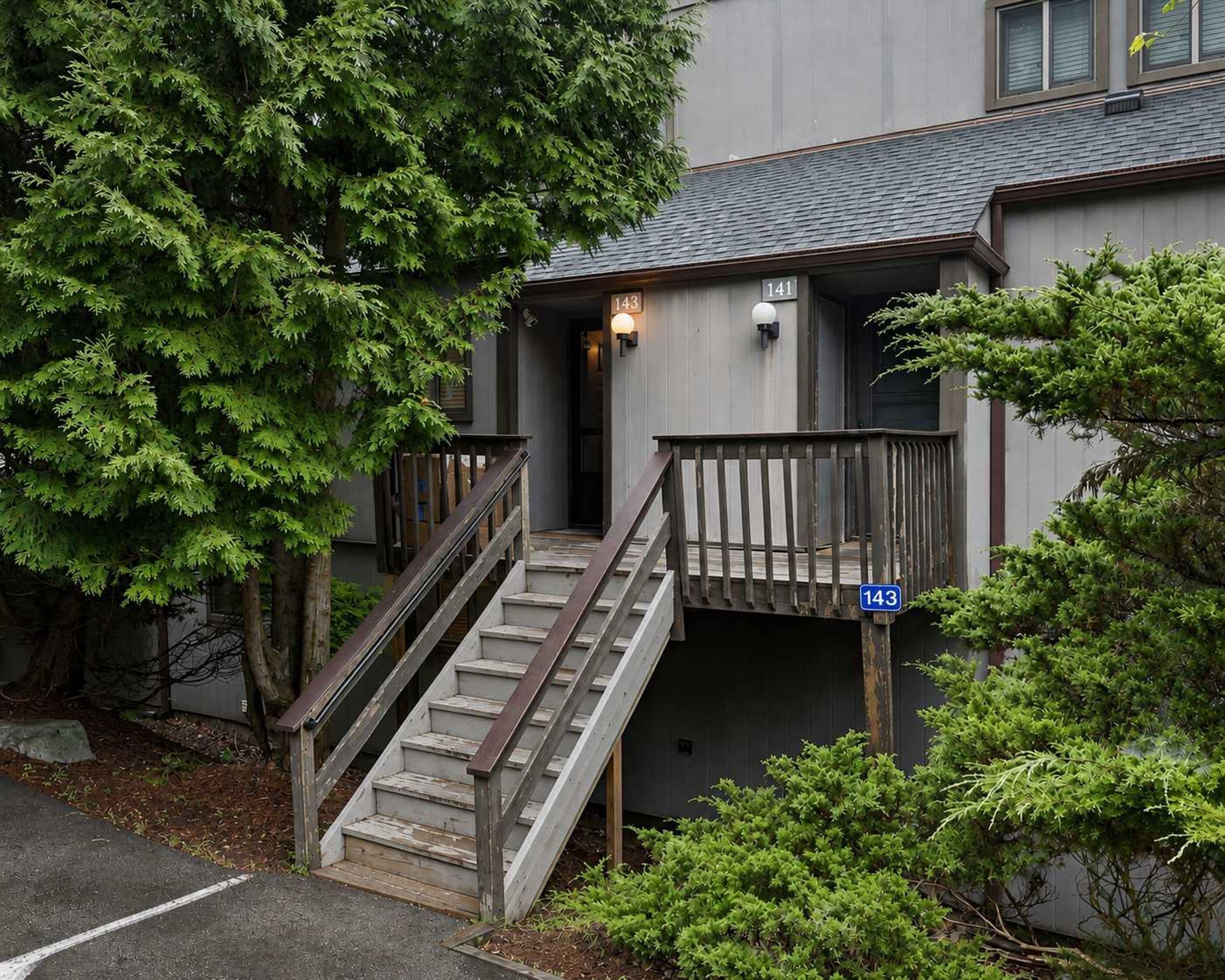 A building with a staircase leading to a porch, surrounded by trees.