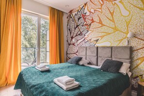 A bedroom with a large bed, a view of trees through a window, and a wall with a geometric pattern.