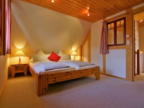 Un dormitorio con una cama de madera, dos lámparas de noche, un cojín rojo y un techo inclinado.