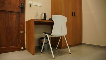 Ein Zimmer mit einem Holzschrank, einem weißen Stuhl, einem Schreibtisch mit Wasserkocher und einem Papierkorb.