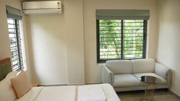 A hotel room with a bed, a sofa, a small table, and a window with blinds.