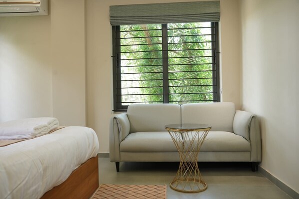 A hotel room with a bed, a sofa, a small round table, and a window with a view of greenery.
