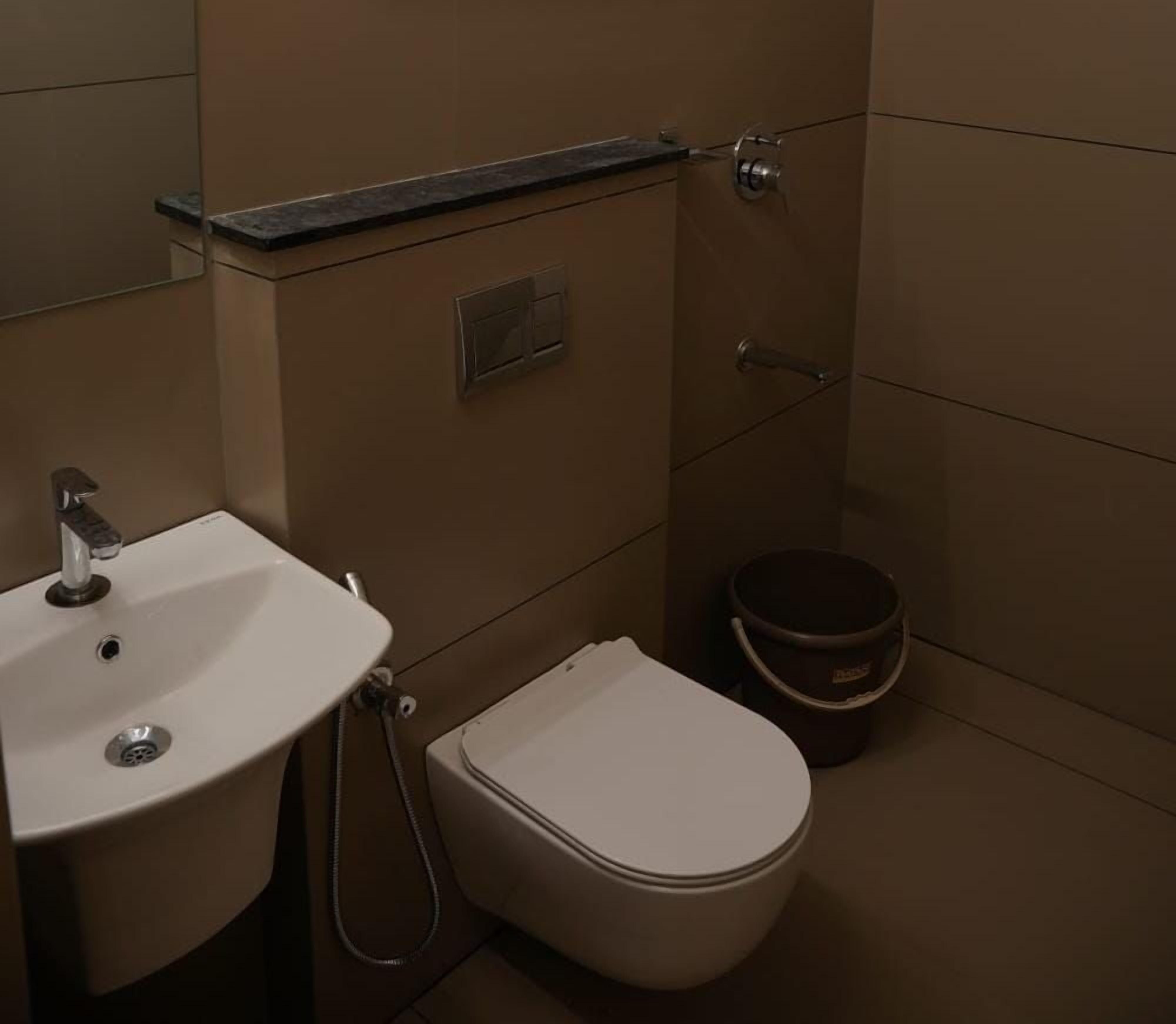 A bathroom with a sink, toilet, and a small bucket.