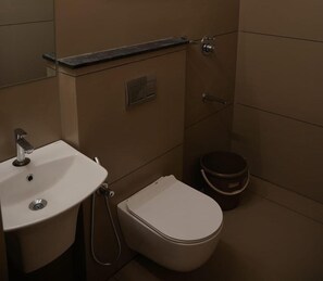 A bathroom with a sink, toilet, and a small bucket.