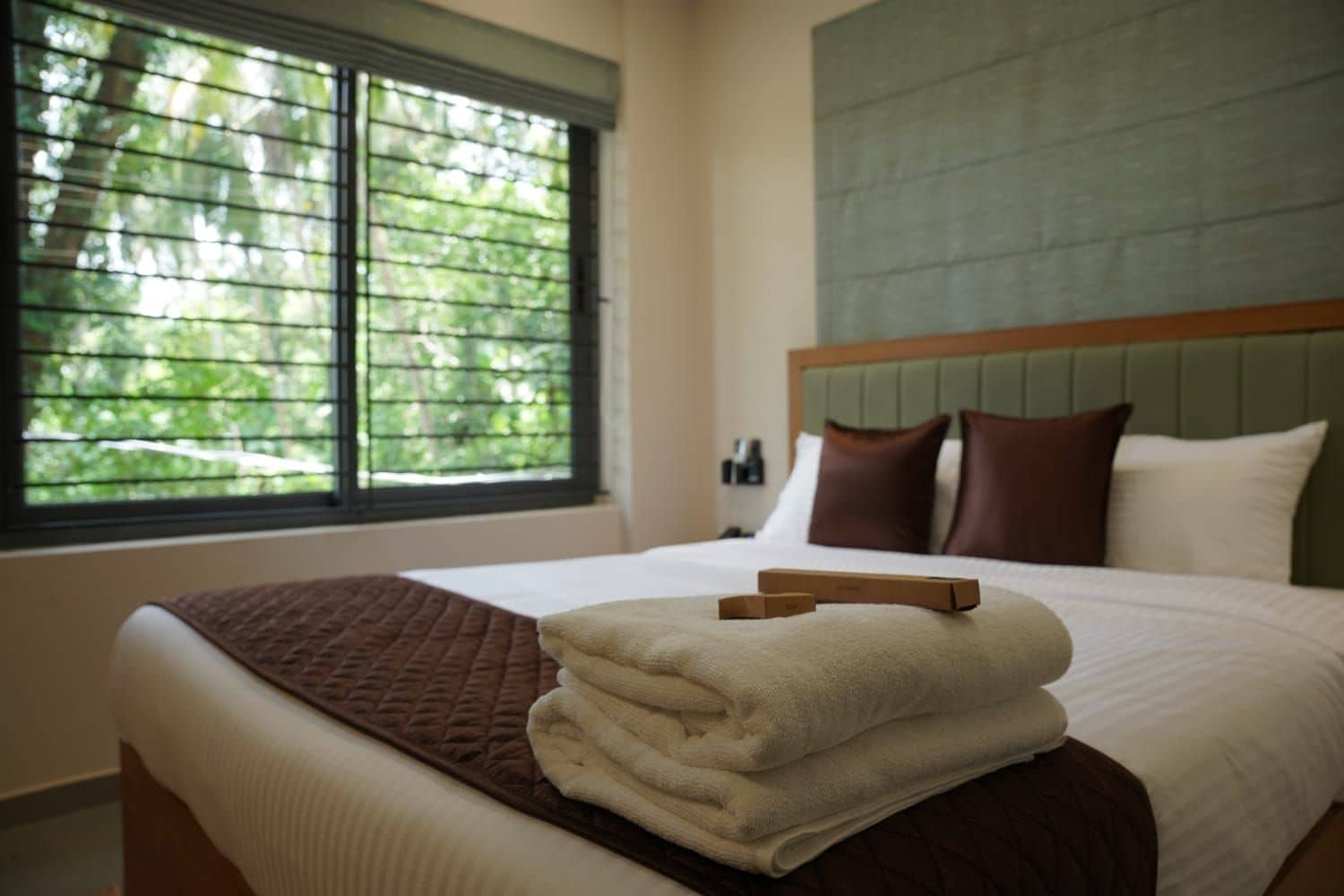 Habitación de hotel con cama, ventana con persianas y vistas a árboles.