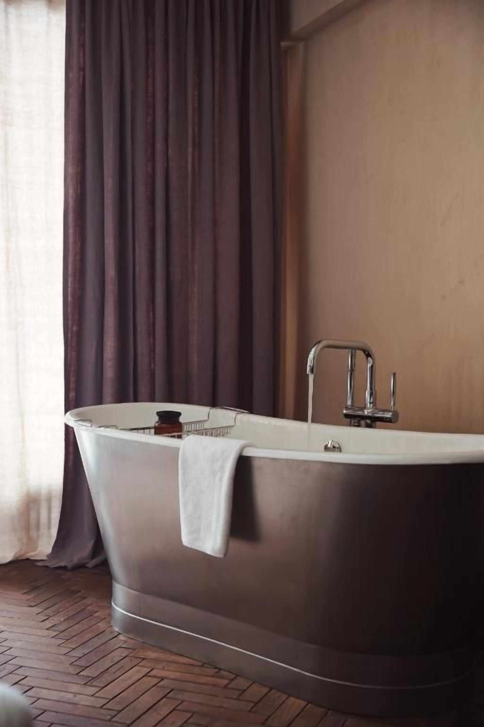 Una bañera independiente en una habitación con piso de madera y una cortina.
