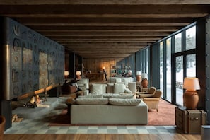 Un salon spacieux avec un grand canapé, plusieurs fauteuils et une cheminée. On y trouve une bibliothèque remplie de livres et une grande fenêtre qui offre une vue sur l’extérieur.