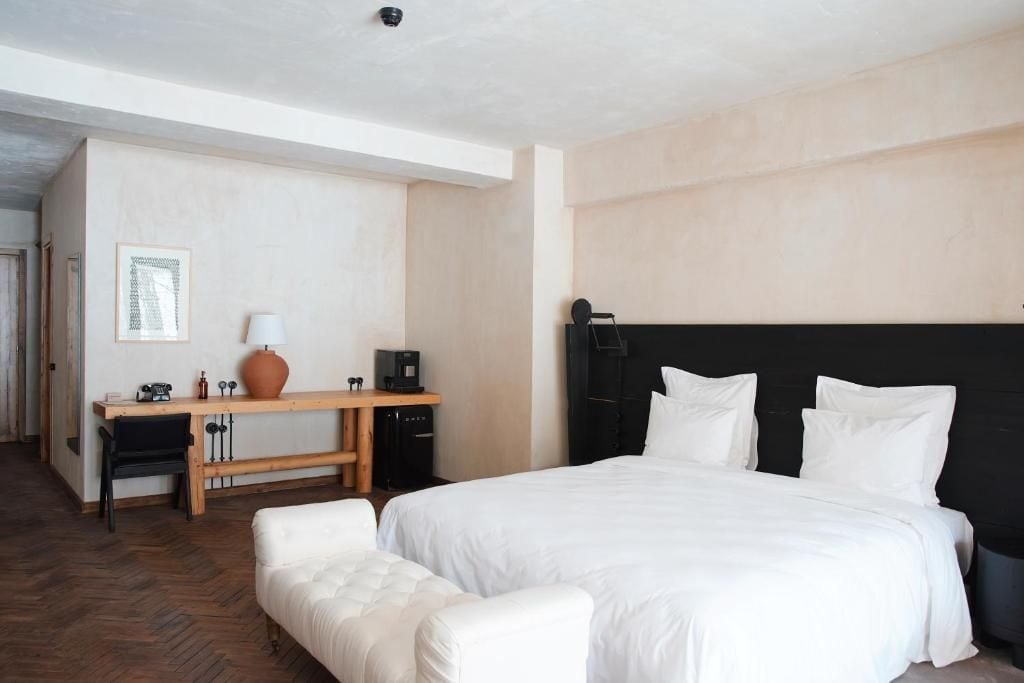A hotel room with a large bed, a desk with a chair, a coffee machine, and a vase.