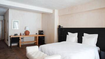 A hotel room with a large bed, a desk with a chair, a coffee machine, and a vase.