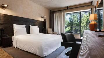 A hotel room with a large bed, a desk, a chair, and a window with curtains.
