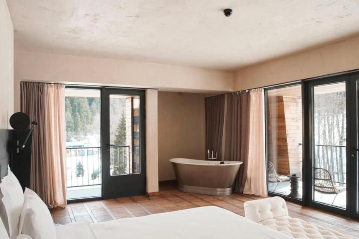 Une chambre avec un grand lit, une baignoire et un balcon avec des rideaux.