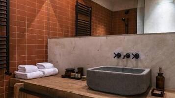 Une salle de bain avec un lavabo en pierre, des étagères en bois et un sol carrelé.