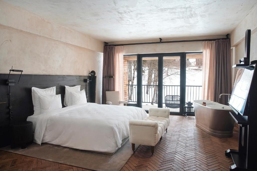 Habitación de hotel con una cama grande, zona de estar, bañera y balcón con vistas.