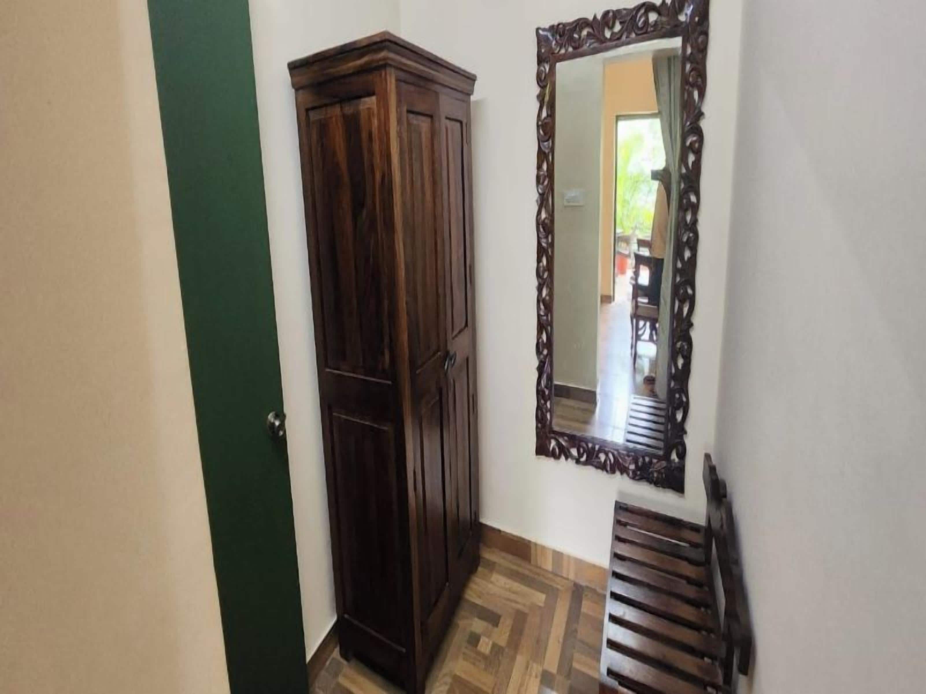 Un pasillo con un armario de madera, un espejo con marco decorativo y un banco.