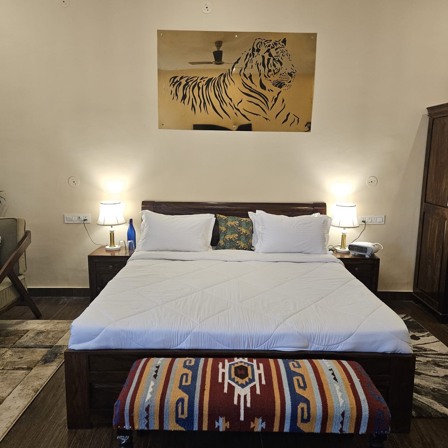 A hotel room with a large bed, two bedside lamps, a wall-mounted tiger artwork, and a patterned bench.